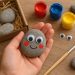 Hand-painted pet rock with googly eyes and colorful decorations on a wooden surface